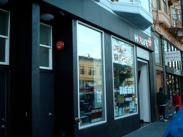 A close-up view of the entrance to &ldquo;HOUSE,&rdquo; a modern storefront with large glass windows framed in black. The interior is visible through the windows.